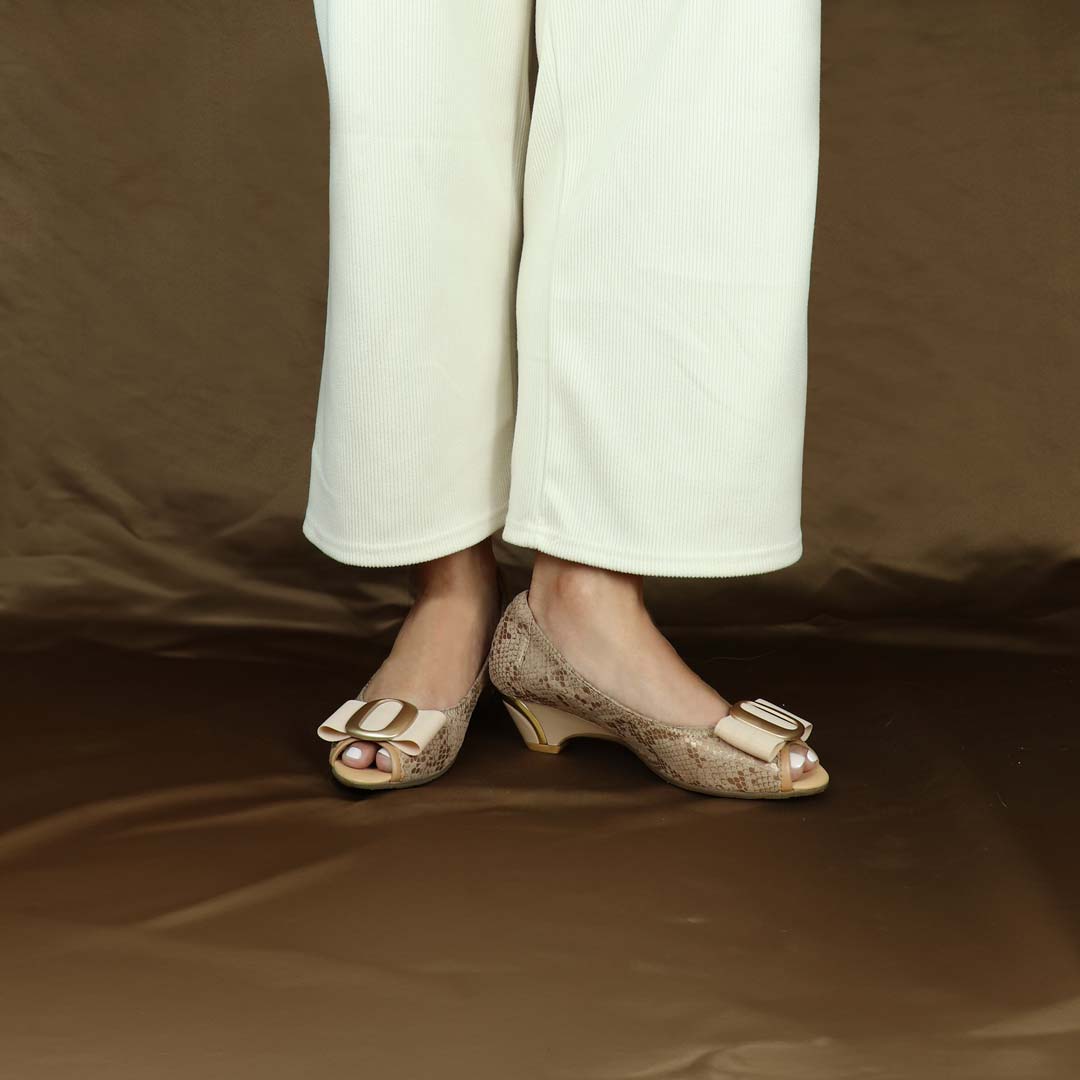 A model showcasing Thomas Chan's Vintage Print Pumps with Ribbon Buckle in apricot cream color, featuring an arch-support footbed, standing against a chocolate backdrop.