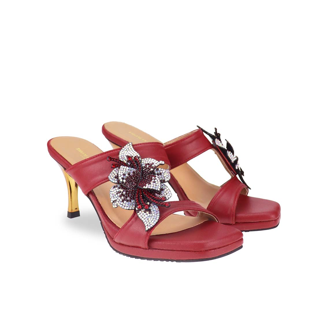 Diagonal view of Thomas Chan's Embellished Flower High Heeled Sandals in red, highlighting the intricately adorned floral decorations and a sophisticated 3-inch gold stiletto heel, set against a clean, white backdrop.