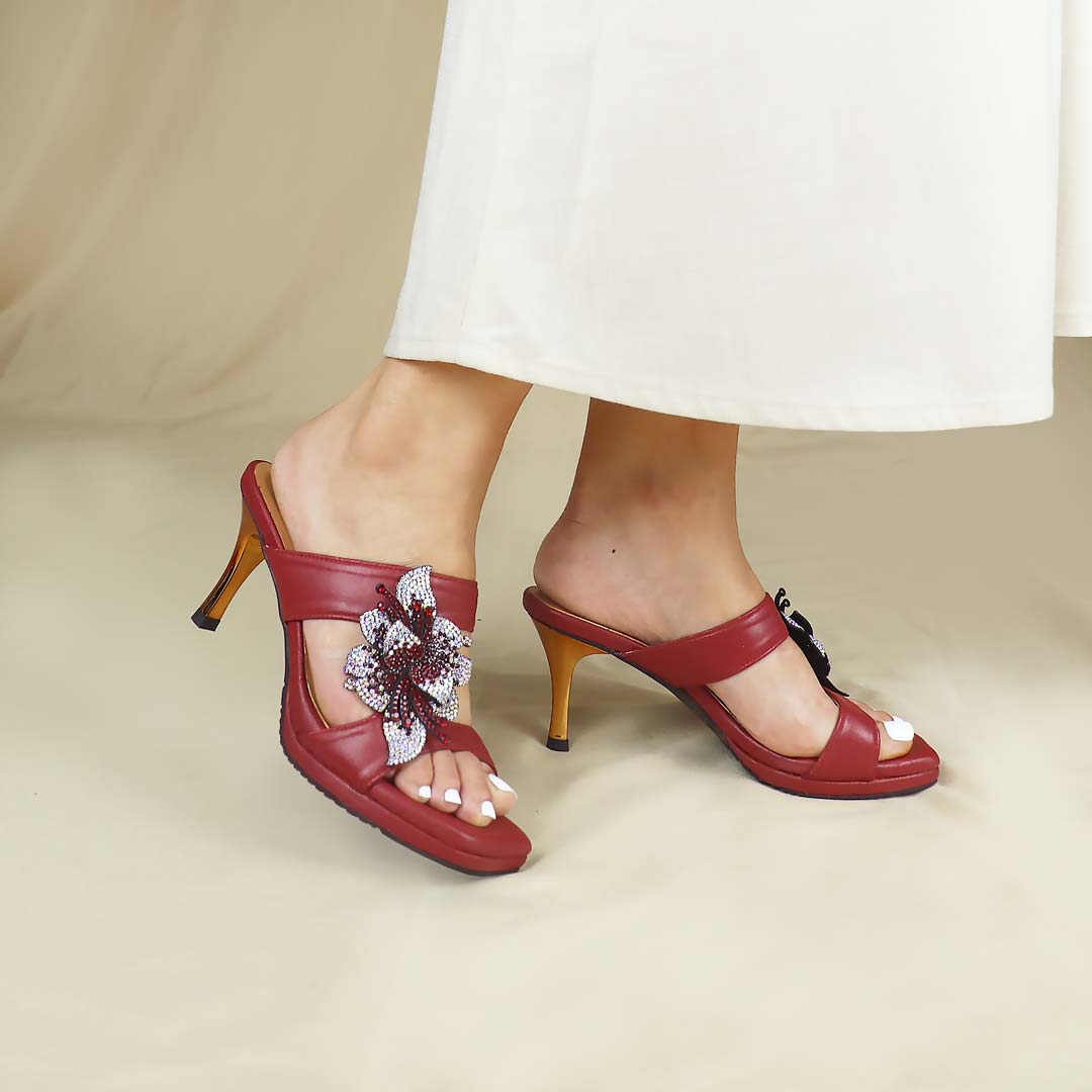 A model standing gracefully, showcasing Thomas Chan's Embellished Flower High Heeled Sandals in red. The design features intricately adorned floral decorations and a refined 3-inch gold stiletto heel, set against a minimalist backdrop. These sandals effortlessly elevate evening events, galas, or any special occasion with sophistication and charm.