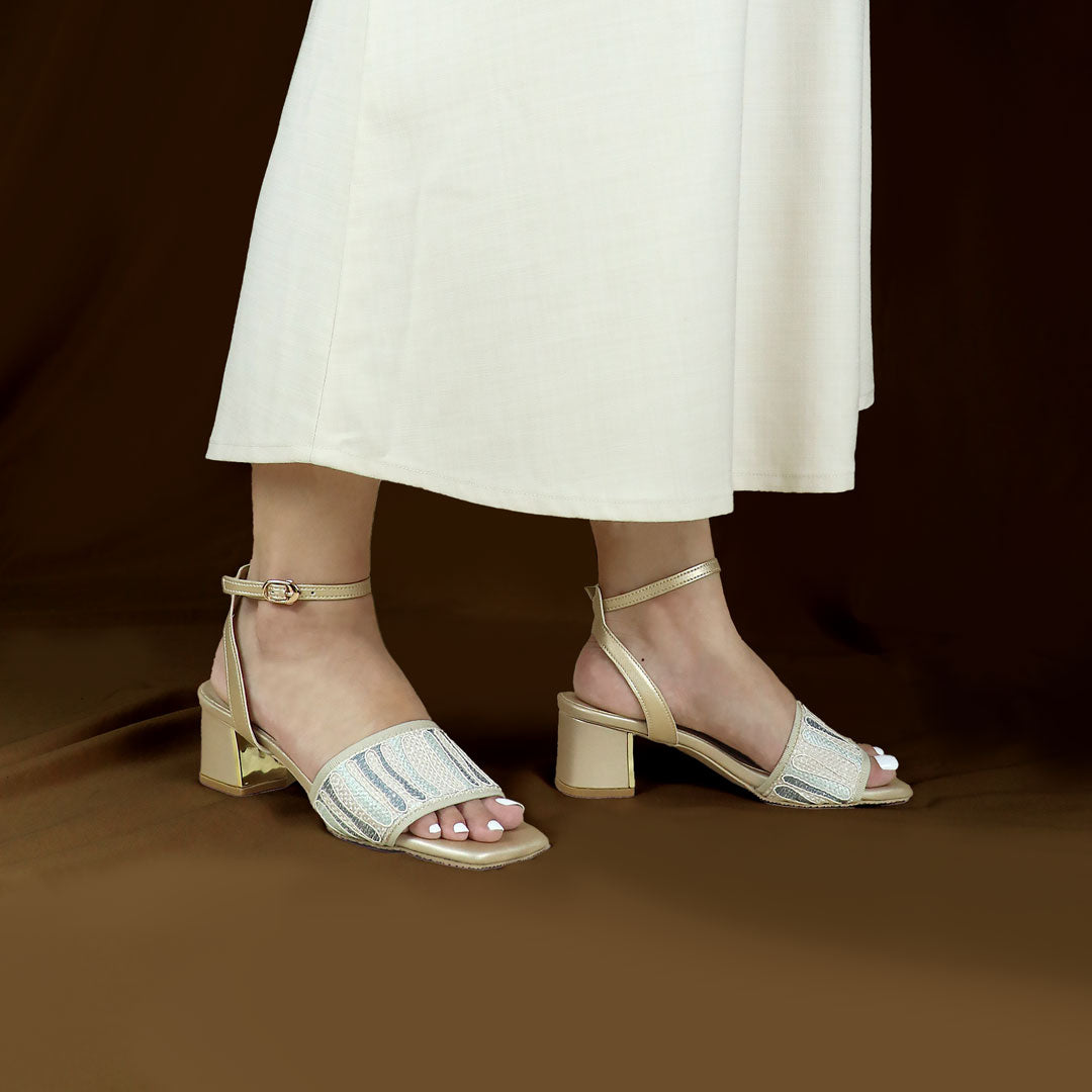 A model standing elegantly, wearing Thomas Chan's Dreamy Boho Ankle Strap Heeled Sandals in light gold, showcasing the intricately embroidered boho wide strap, secure ankle closure, and 5cm uniquely crafted heel, set against a simple backdrop. Perfect for casual outings or events, they blend elegance with everyday practicality.