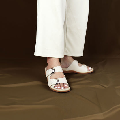 Model wearing size 37 Thomas Chan's Duo Buckle Slide-One flat sandals in ivory from the front view, standing. The sandals feature a comfort footbed with a 3cm flat platform. Behind the model is a bronze-colored backdrop.