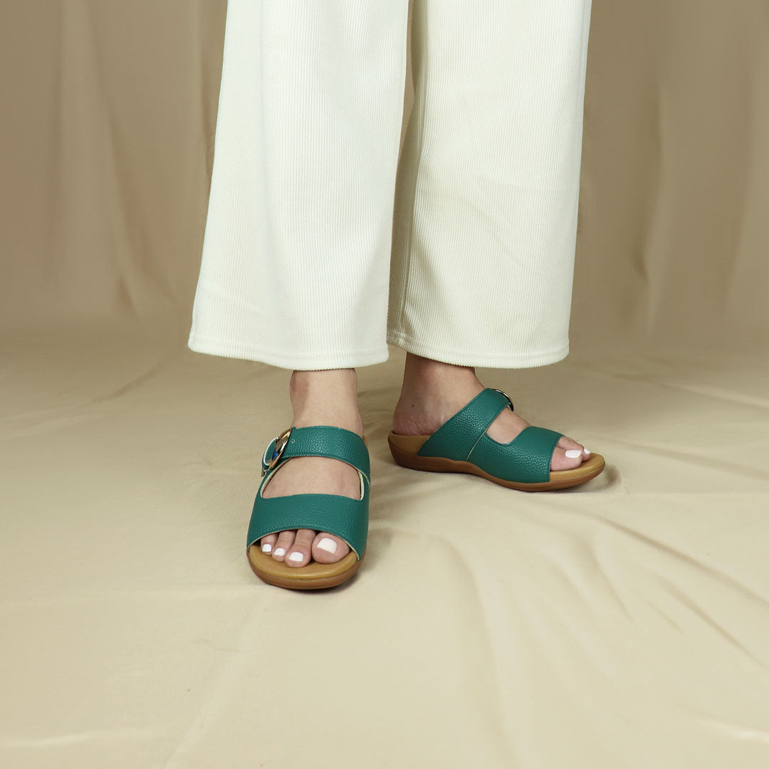 Model wearing size 37 Thomas Chan's Great Coverage Buckle flat sandals in turquoise green cream from the front view, standing. The sandals feature a comfort footbed with a 3cm flat platform. Behind the model is a beige-coloured backdrop.