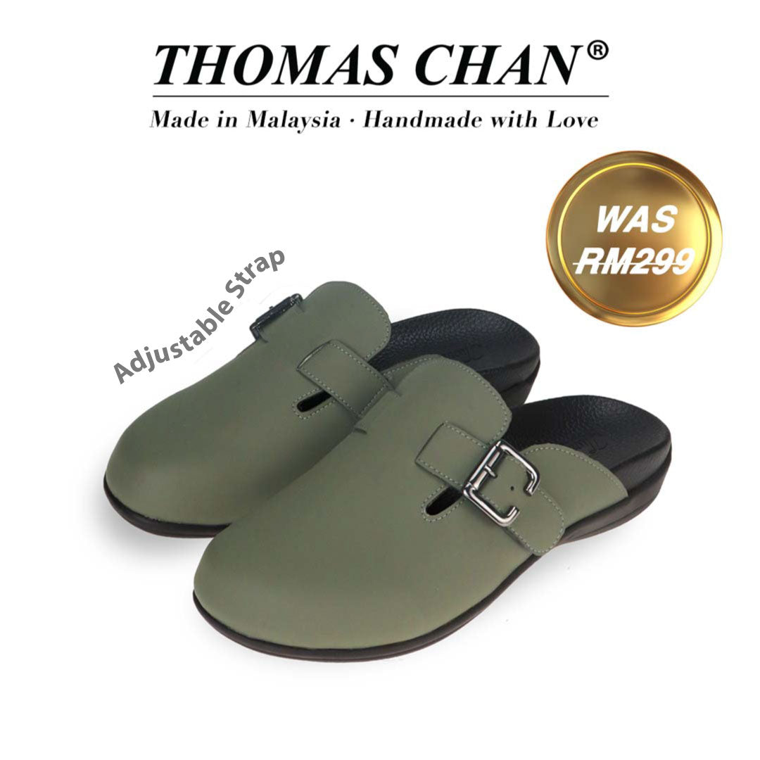 The image features a khaki closed-toe slip-on sandal with a buckle on the side and an arch-support footbed. The top of the image displays the brand name "THOMAS CHAN®" with the text "Made in Malaysia · Handmade with Love" below it. There is a gold and white banner on the right side that says "Was RM299." The sandals also feature an adjustable strap.