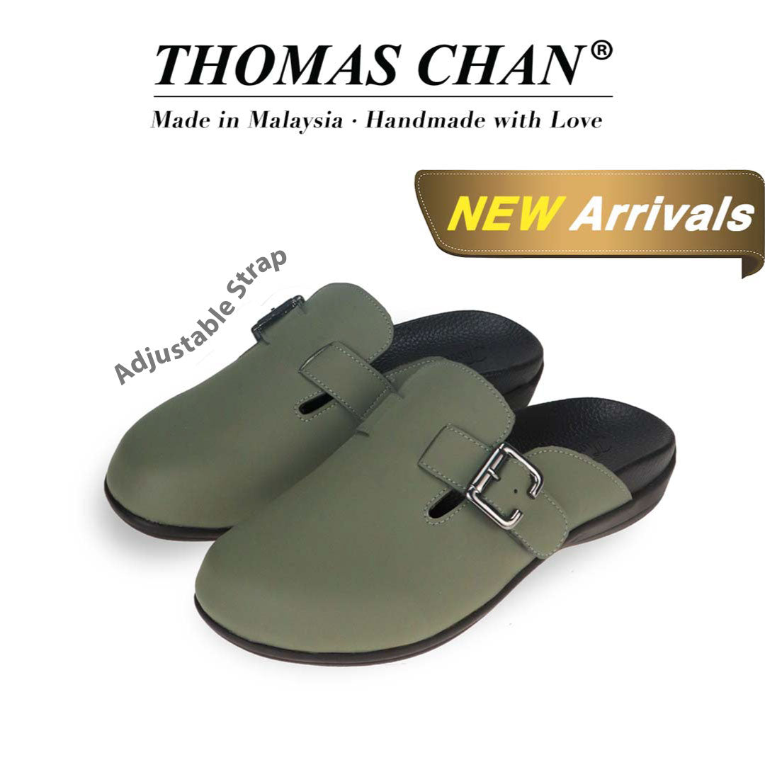 The image features a khaki closed-toe slip-on sandal with a buckle on the side and an arch-support footbed. The top of the image displays the brand name "THOMAS CHAN®" with the text "Made in Malaysia · Handmade with Love" below it. There is a gold and white banner on the right side that says "NEW Arrivals." The sandals also feature an adjustable strap.