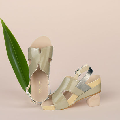 The image shows a pair of stylish ivory green orthotic wedges. These shoes feature a unique H-strap with slingback design, providing both elegance and comfort. The wedges are from Thomas Chan Malaysia, as indicated by the branding inside the shoe. The setting is enhanced by the presence of a leaf in the light cream background, giving the image a casual and delicate feel.