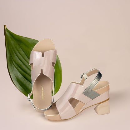 The image shows a pair of stylish light taupe orthotic wedges. These shoes feature a unique H-strap with slingback design, providing both elegance and comfort. The wedges are from Thomas Chan Malaysia, as indicated by the branding inside the shoe. The setting is enhanced by the presence of a leaf in the light cream background, giving the image a casual and delicate feel.