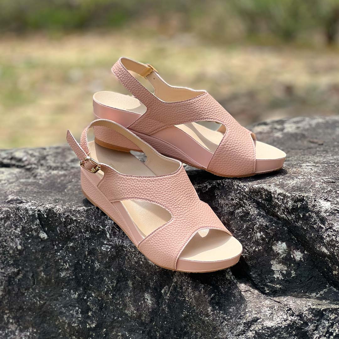 Thomas Chan Daily Wear Slingback Low Wedges in rosy pink displayed outdoors on a rock surface. The sandals feature a textured pebbly lychee print, an elegant slingback design with a buckle closure, and a comfortable low wedge heel. The 'THOMAS CHAN®' brand is visible on the footbed.