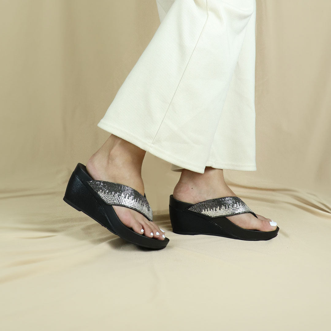 Model wearing Suede Rhinestone Wedge Flip Flops in black. Featuring a 3-inch wedge heel, these sandals provide exceptional comfort with the integrated Thomas Chan® Orthotic Arch-Legance footbed, set against a cream backdrop for a refined and elegant presentation.