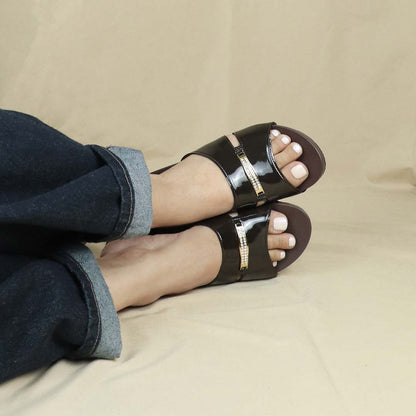 Model showcasing Thomas Chan Mini Charm Low Wedge Sandals in dark chocolate, featuring a delicate charm detail, full coverage design, and arch-support footbed, set against a cream backdrop.