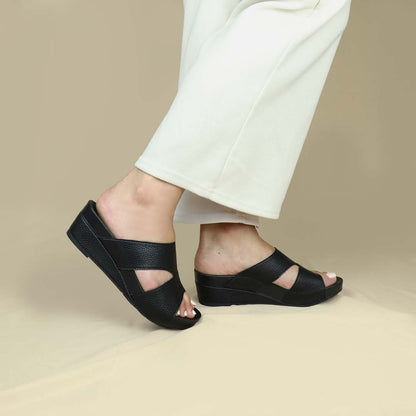 Model wearing Pebble Lychee Everyday Low Wedge Slides in black from side view. Featuring a 2-inch wedge heel, these sandals provide exceptional comfort with the integrated Thomas Chan® Orthotic Arch-Legance footbed. 