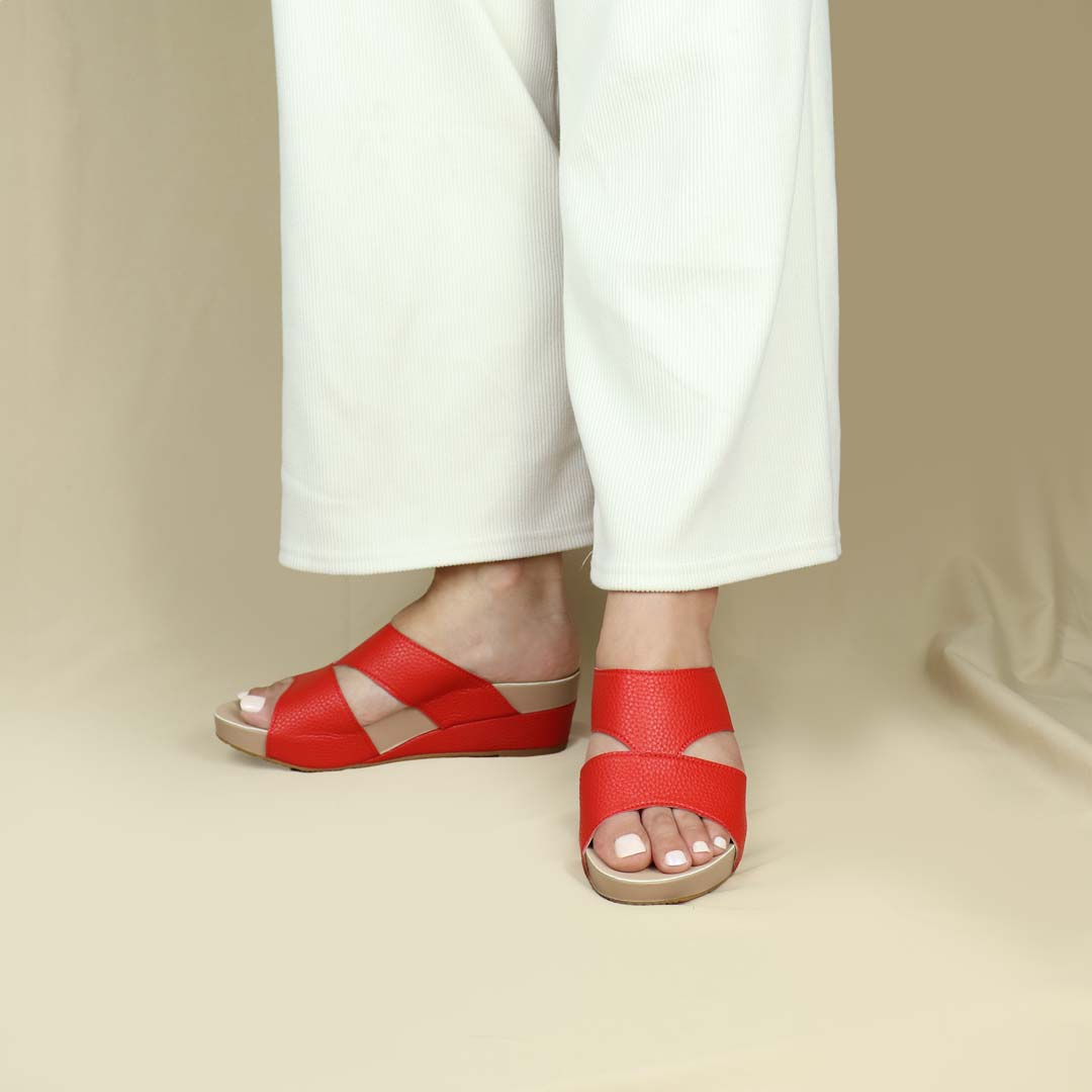 Model wearing Pebble Lychee Everyday Low Wedge Slides in red. Featuring a 2-inch wedge heel, these sandals provide exceptional comfort with the integrated Thomas Chan® Orthotic Arch-Legance footbed. 