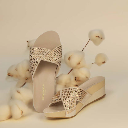 A pair of stylish Diamond Crisscross Suede Low Wedges in creamy gold with a crisscross design adorned with rectangular diamonds, offering both elegance and comfort. The shoes are branded Thomas Chan Malaysia. The scene is enhanced by cotton flowers against a light yellow background, creating a minimal and whimsical atmosphere.