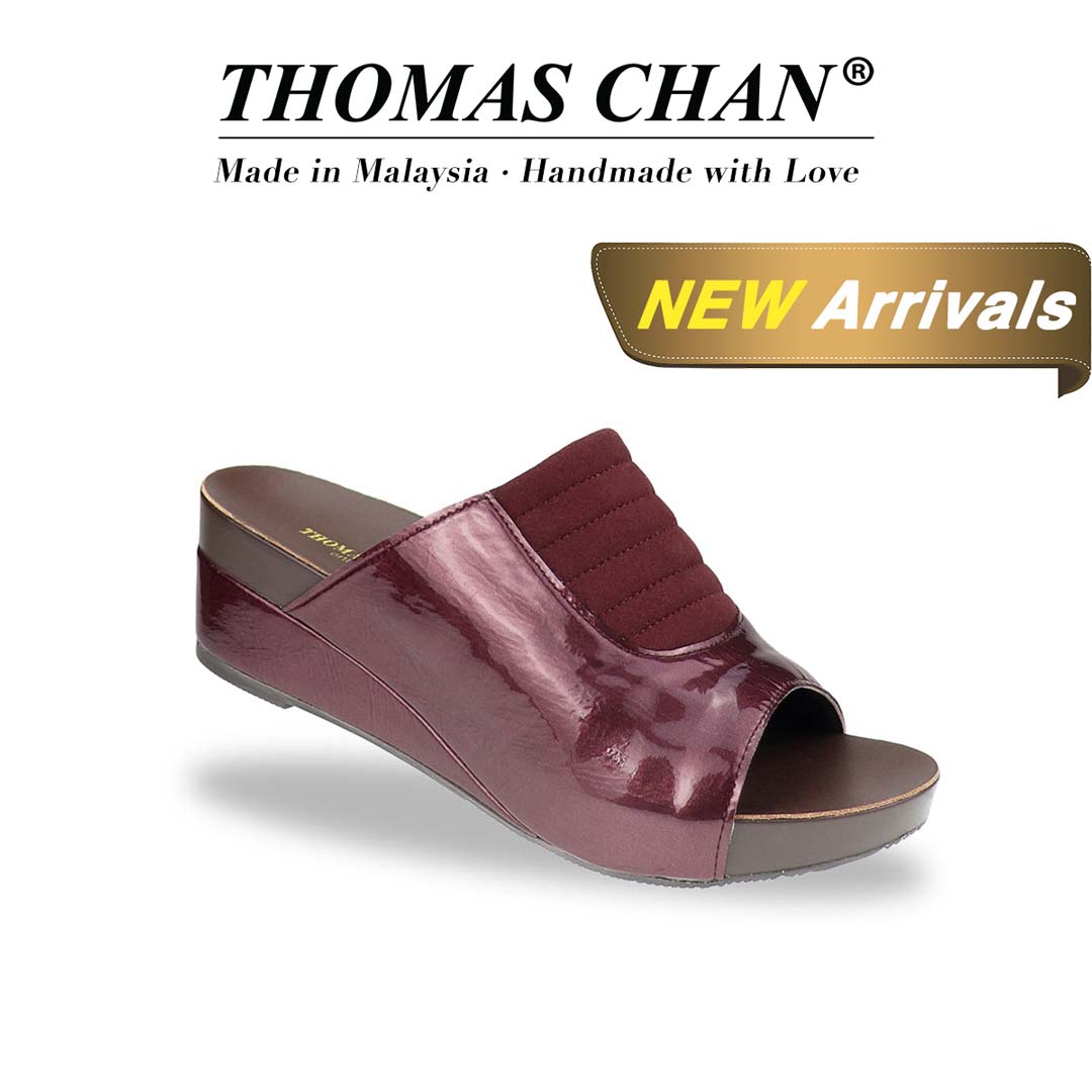 Diagonal view of Thomas Chan's Matte Cushioned Low Wedge Sandals in maroon, showcasing matte leather front padding, pattern leather accents, and the signature arch-support footbed for all-day comfort and style. "THOMAS CHAN®" brand displayed with "Made in Malaysia · Handmade with Love" below. Gold and white banner highlights special offer: "NEW ARRIVAL."