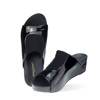 Full view of Thomas Chan's Matte Cushioned Low Wedge Sandals in black, highlighting the matte leather front padding, pattern leather accents, and signature arch-support footbed for all-day comfort and style. Set outdoors on a cement floor with lush grass in the background.