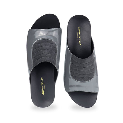 Front view of Thomas Chan's Matte Cushioned Low Wedge Sandals in grey, highlighting the matte leather front padding, pattern leather accents, and signature arch-support footbed for all-day comfort and style. Set outdoors on a cement floor with lush grass in the background.