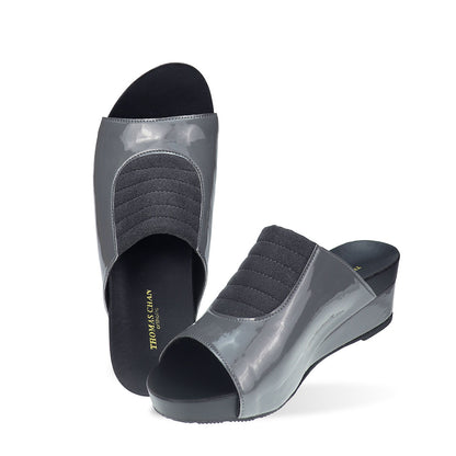 Full view of Thomas Chan's Matte Cushioned Low Wedge Sandals in grey, highlighting the matte leather front padding, pattern leather accents, and signature arch-support footbed for all-day comfort and style. Set outdoors on a cement floor with lush grass in the background.