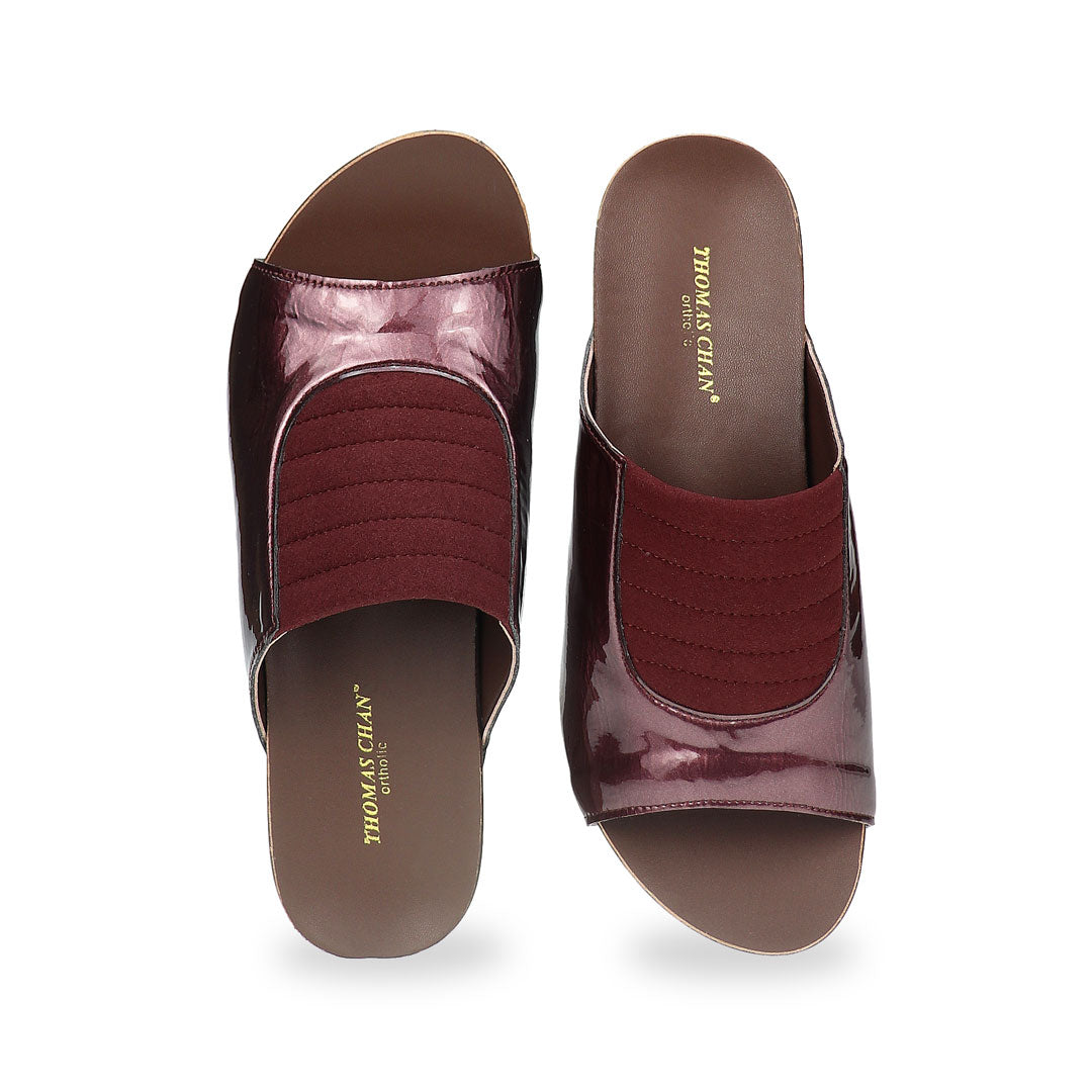 Front view of Thomas Chan's Matte Cushioned Low Wedge Sandals in maroon, highlighting the matte leather front padding, pattern leather accents, and signature arch-support footbed for all-day comfort and style. Set outdoors on a cement floor with lush grass in the background.