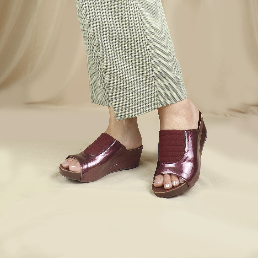  Model showcasing Thomas Chan's Matte Cushioned Low Wedge Sandals in maroon, featuring matte leather front padding, pattern leather accents, and a 2-inch arch-support wedge for stylish all-day comfort, elegantly presented against a cream backdrop.