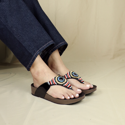 A model wearing black Thomas Chan's Boho Beaded Flatform Flip-Flops with a 3cm flatform, paired with jeans. Set against a cream-colored backdrop, highlighting the flip-flops' boho beaded design and casual style.