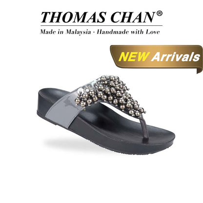 Diagonal view of Thomas Chan's Pearl Tassel Flip-Flops from the LiteStep Collection. The sandals feature a glossy grey strap adorned with pearl tassel embellishments, paired with a comfortable flatform sole. The 'THOMAS CHAN®' brand is displayed below with 'Made in Malaysia · Handmade with Love.' A gold and white banner highlights a special offer: 'New Arrival'