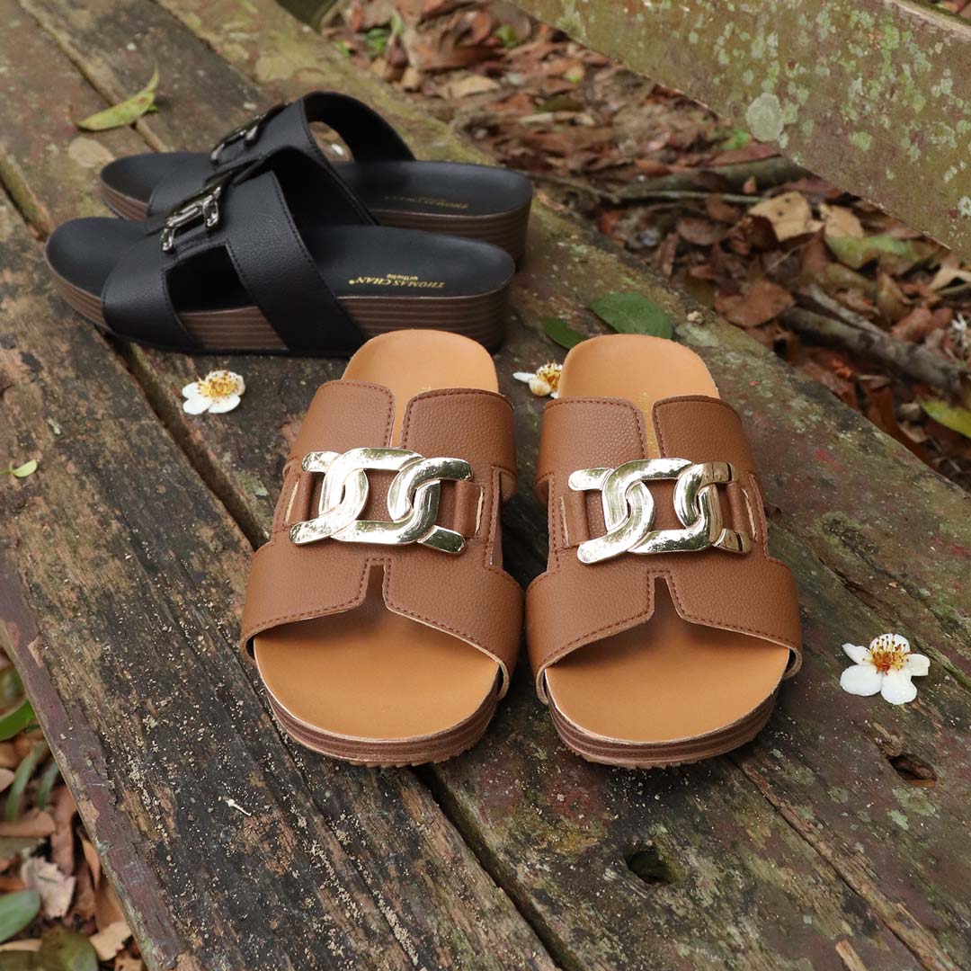 Thomas Chan's Metallic Buckle H-Flatform Sandals in camel, featuring a bold metallic buckle across the H-strap and LiteStep flatform footbed, displayed outdoors on a weathered wooden bench with floral accents.