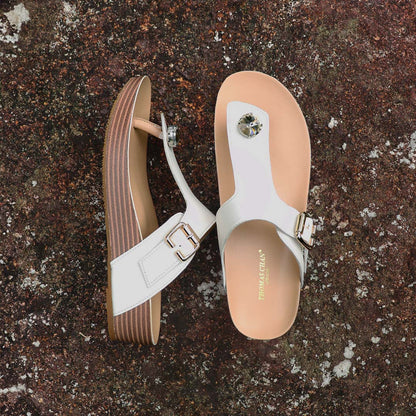 Full view of Thomas Chan’s Dazzle Crystal Adjustable Flip-Flops in ivory, placed on a red stone outdoors. The image showcases the sparkling crystal stone, adjustable buckle strap, and LiteStep flatform footbed, emphasizing their casual yet elegant style.