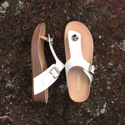 Full view of Thomas Chan’s Dazzle Crystal Adjustable Flip-Flops in ivory, placed on a red stone outdoors. The image showcases the sparkling crystal stone, adjustable buckle strap, and LiteStep flatform footbed, emphasizing their casual yet elegant style.