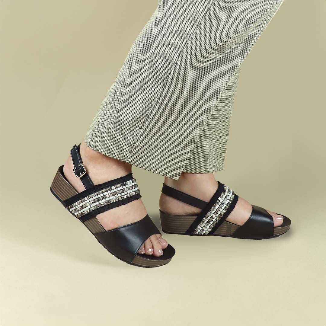 Side-angle view of Thomas Chan’s Summer Love Duo-Strap Slingback Sandals in black, showcased by a model against a cream studio backdrop, highlighting the elegant duo straps, a secure slingback design, and a LiteStep flatform sole with light arch support.