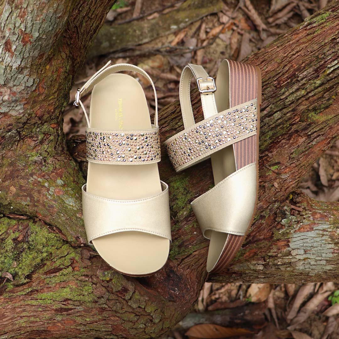 Full view of Thomas Chan’s Summer Love Duo-Strap Slingback Sandals in gold, placed on a fallen wood surface. The image highlights the elegant duo straps, secure slingback design, and LiteStep flatform sole with light arch support, emphasizing their casual yet sophisticated style.