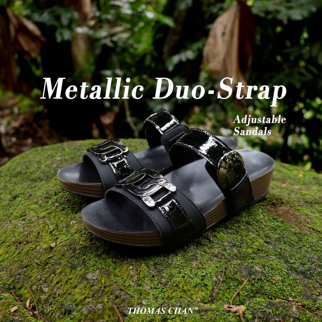 
Full diagonal view of Thomas Chan’s Metallic Duo-Strap Adjustable Sandals in black, placed on a green moss-covered stone outdoors. The image highlights sleek metallic straps with a decorative buckle at the front, an adjustable instep buckle strap for a customizable fit, and a LiteStep flatform footbed, emphasizing their casual yet elegant style. The words 'Metallic Duo-Strap' and 'Adjustable Sandals' are prominently displayed, with the 'Thomas Chan' logo positioned at the bottom.