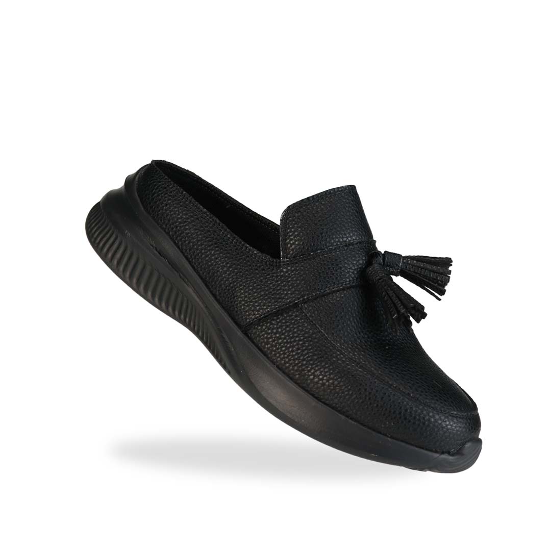 Diagonal view of Thomas Chan Feather-Light Tassel Slide-On Loafers in black, featuring a tassel bell design and a comfortable cushioned footbed.