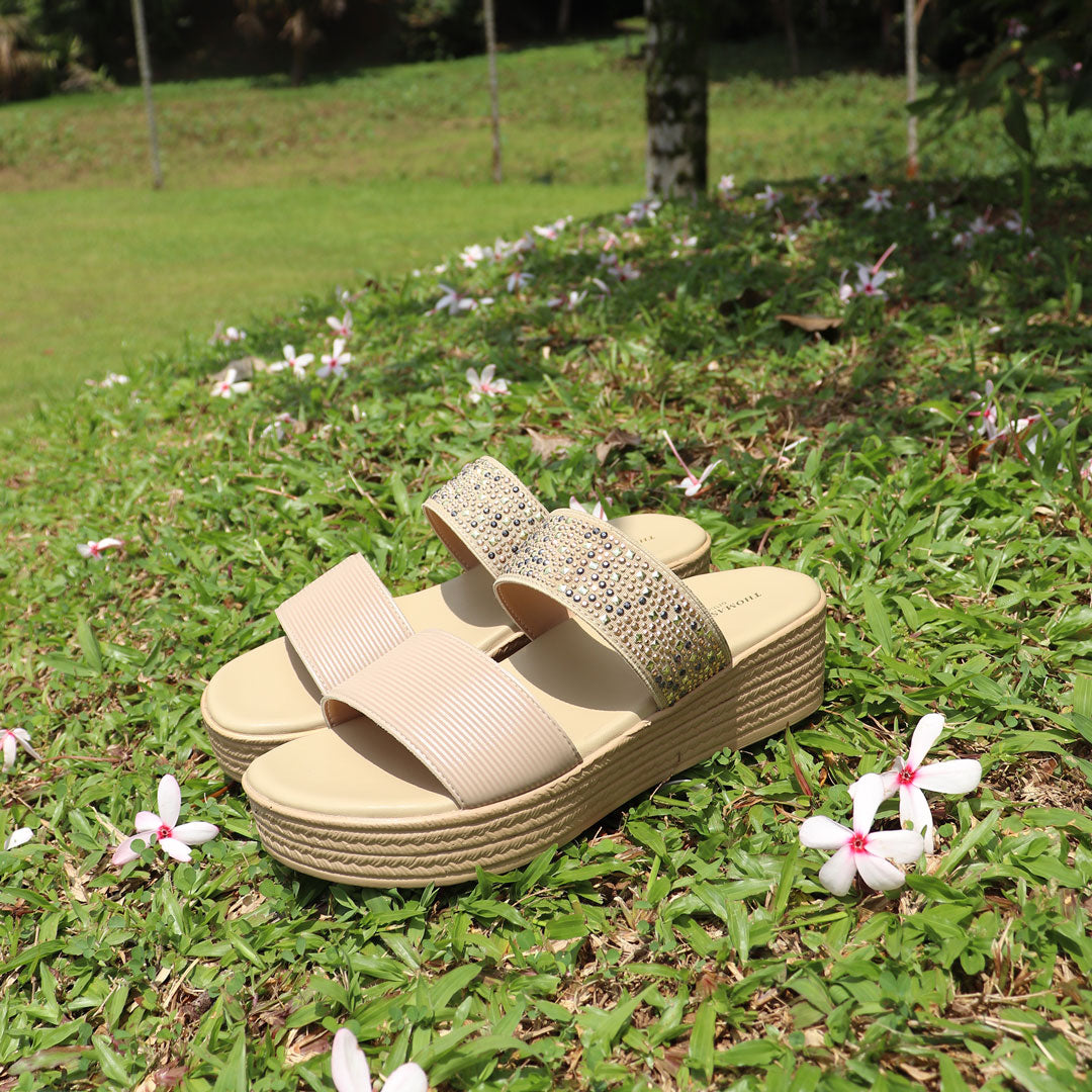 Cream-colored Thomas Chan boho rhinestone flatform sandals with a comfortable footbed, perfect for a relaxed and comfortable vibe. The platform features a braided design and measures 3cm at the front and 5cm at the back. The photo shows the sandals from the side, set against a green outdoor backdrop with fallen flowers.