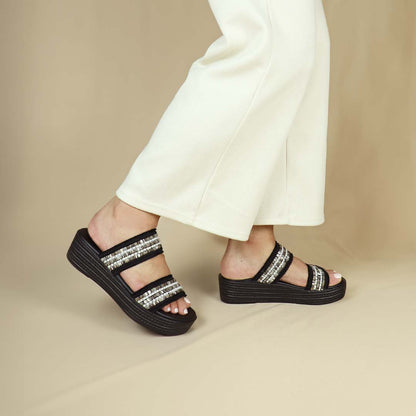 Model wearing size 37 Thomas Chan Summer Love Boho low platform sandals in black with little white embroidery from the side view, featuring a comfort footbed. The platform, with a black braided element, measures 3cm at the front and 5cm at the back.