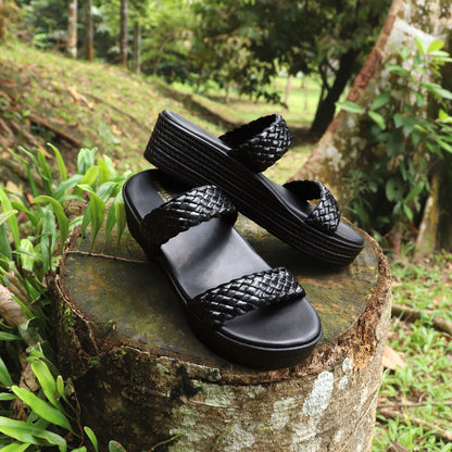 Thomas Chan Pretty Essential Strappy Flatform Sandals in black, showcasing sleek dual braided straps for a chic, modern look. The sandals are set against a natural forest backdrop, highlighting their cushioned flatform sole, expertly designed for both comfort and effortless style.