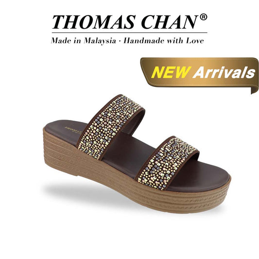 Diagonal view of the Thomas Chan Strappy Rhinestone Flatform Sandals in brown, featuring two elegant rhinestone-adorned straps and a cushioned footbed designed for maximum comfort. The 'THOMAS CHAN®' brand logo is clearly visible, with the inscription 'Made in Malaysia · Handmade with Love' underneath. A gold and white banner showcases the special offer: 'New Arrival.'