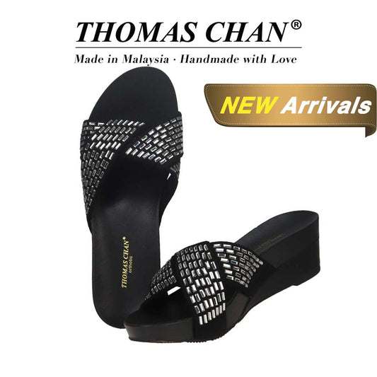 Thomas Chan Diamond Crisscross Suede Low Wedges in black, featuring an elegant design and arch-support footbed. "THOMAS CHAN®" brand displayed with "Made in Malaysia · Handmade with Love" below. Gold and white banner highlights special offer: "New Arrival."