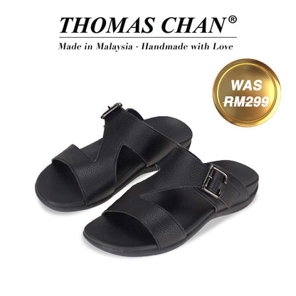 An image of Thomas Chan Men Zig Zag Buckle Sandals in black colour, featuring an arch-support footbed. The top of the image displays the brand name "THOMAS CHAN®" with the text "Made in Malaysia · Handmade with Love" below it. A gold and white banner on the right side states "WAS 299."